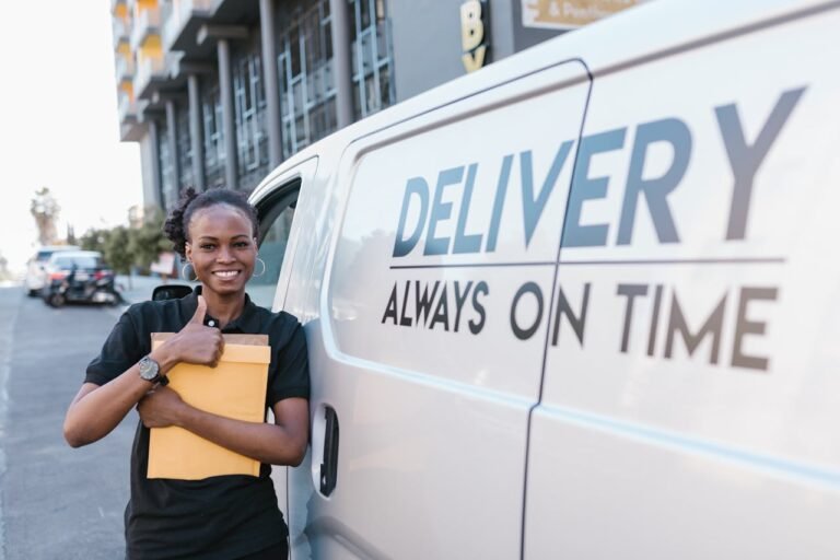 A cheerful delivery woman standing by a van with a parcel, ready for delivery.